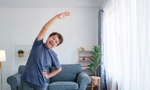 A woman in her 50s stretches at home, smiling