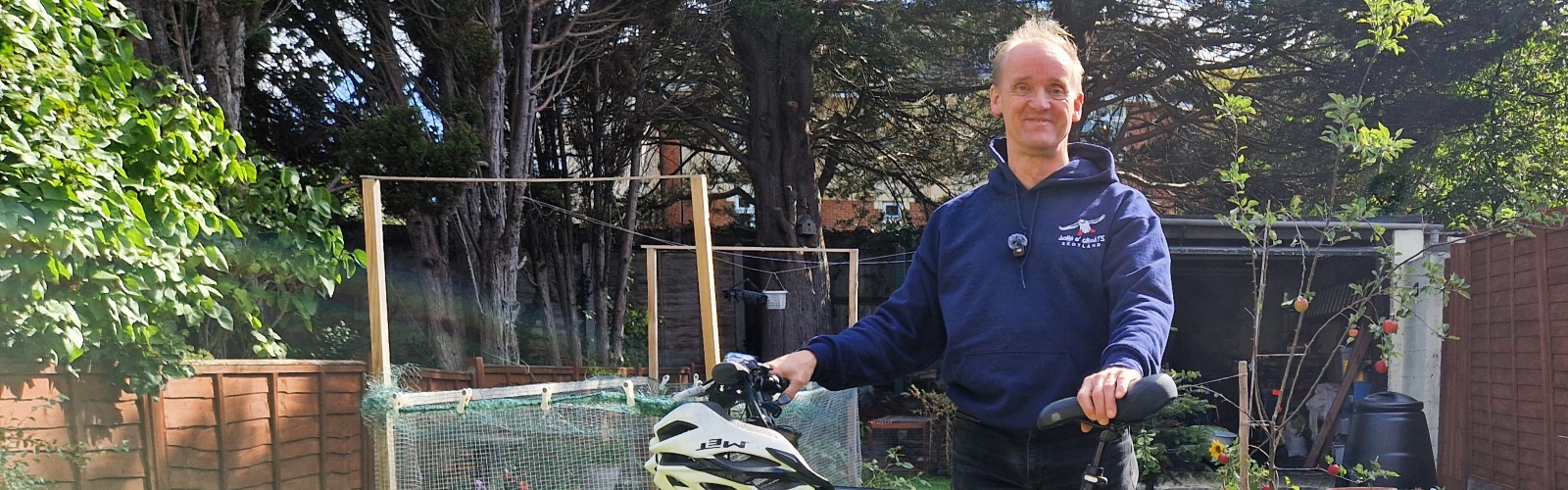 A middle-aged man, standing in his sunny garden with his bike