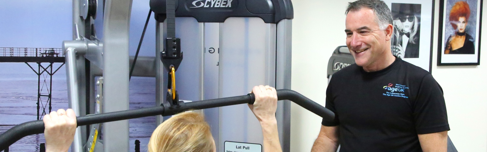 A gym instructor speaks with a woman doing a weight exercise